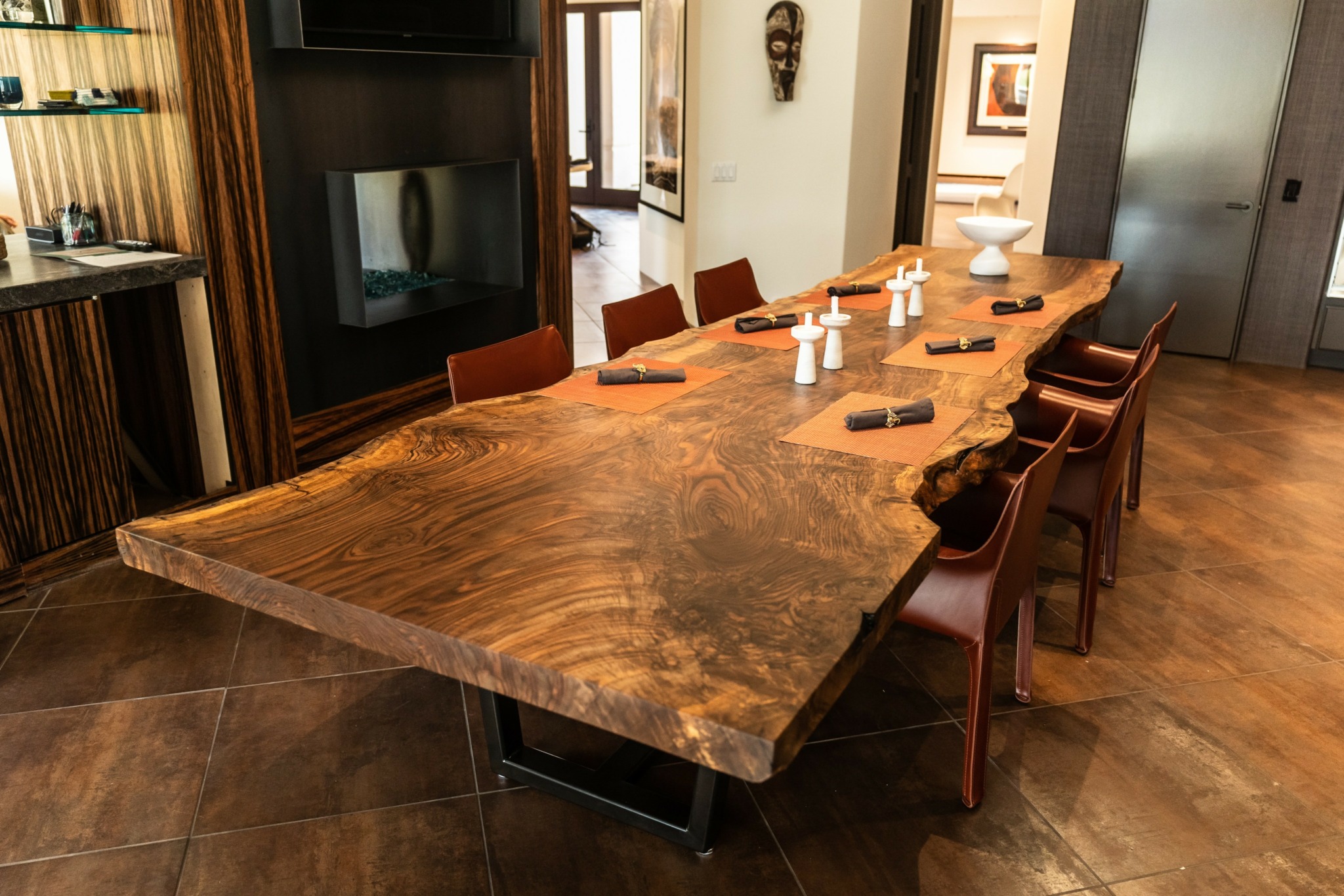 Large wooden dining table with chairs in a room, set with bottles, bowls, and utensils, with a TV and decor in background.