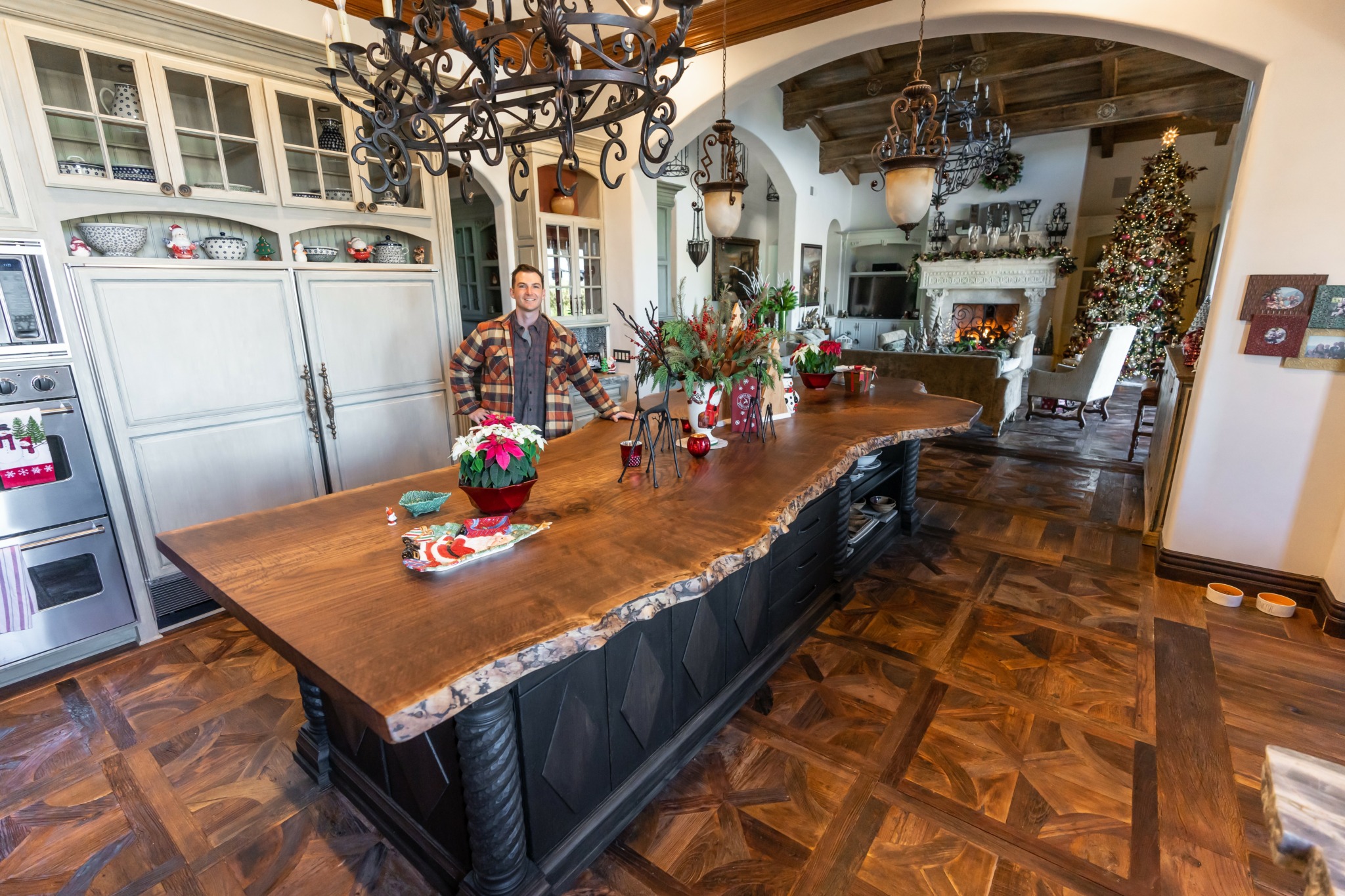 Large wooden dining table with floral centerpiece in a decorated room, chandelier overhead, and a person standing nearby.