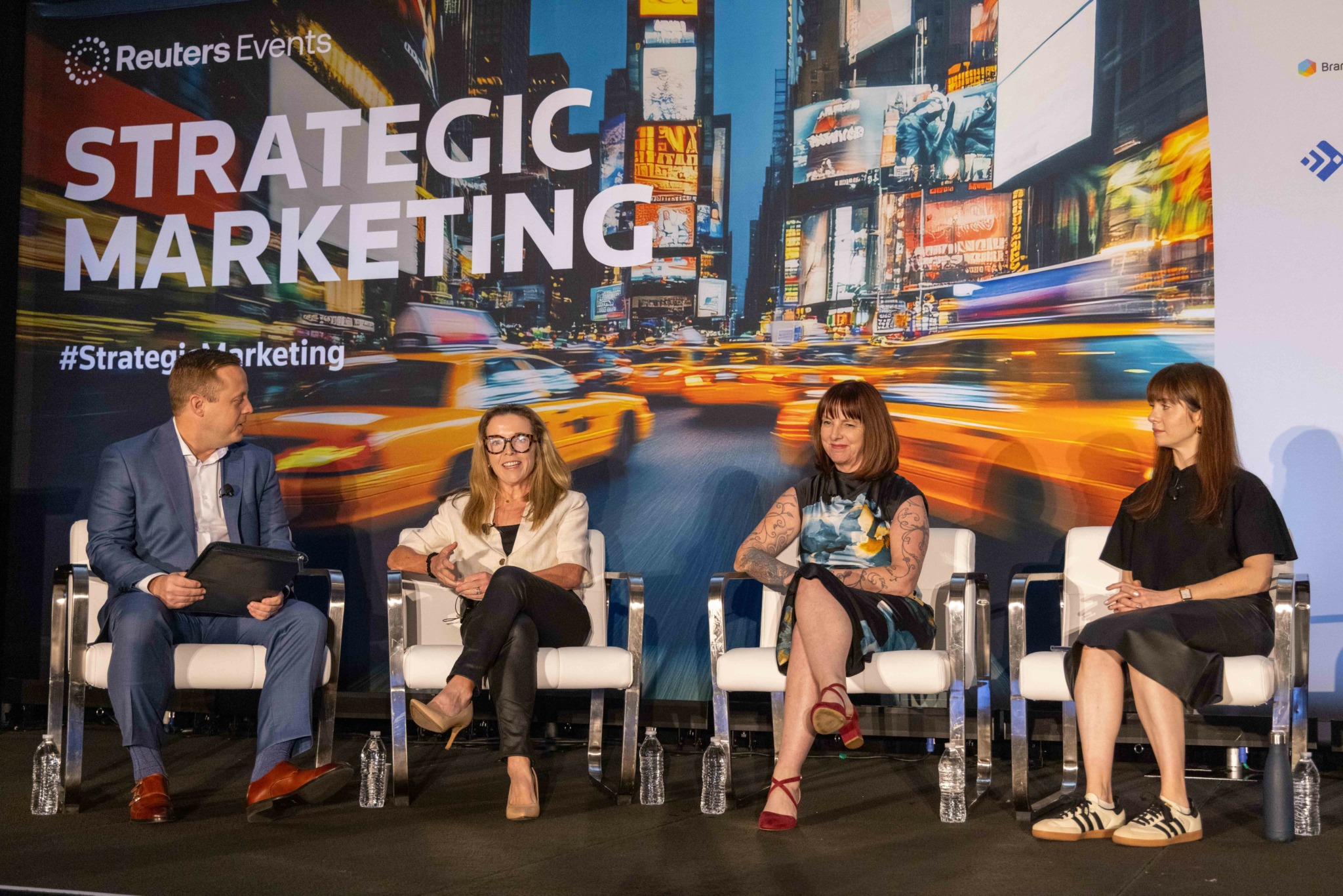 Four people seated on stage in front of a large screen displaying 'Strategic Marketing' and cityscape background, engaging in discussion.