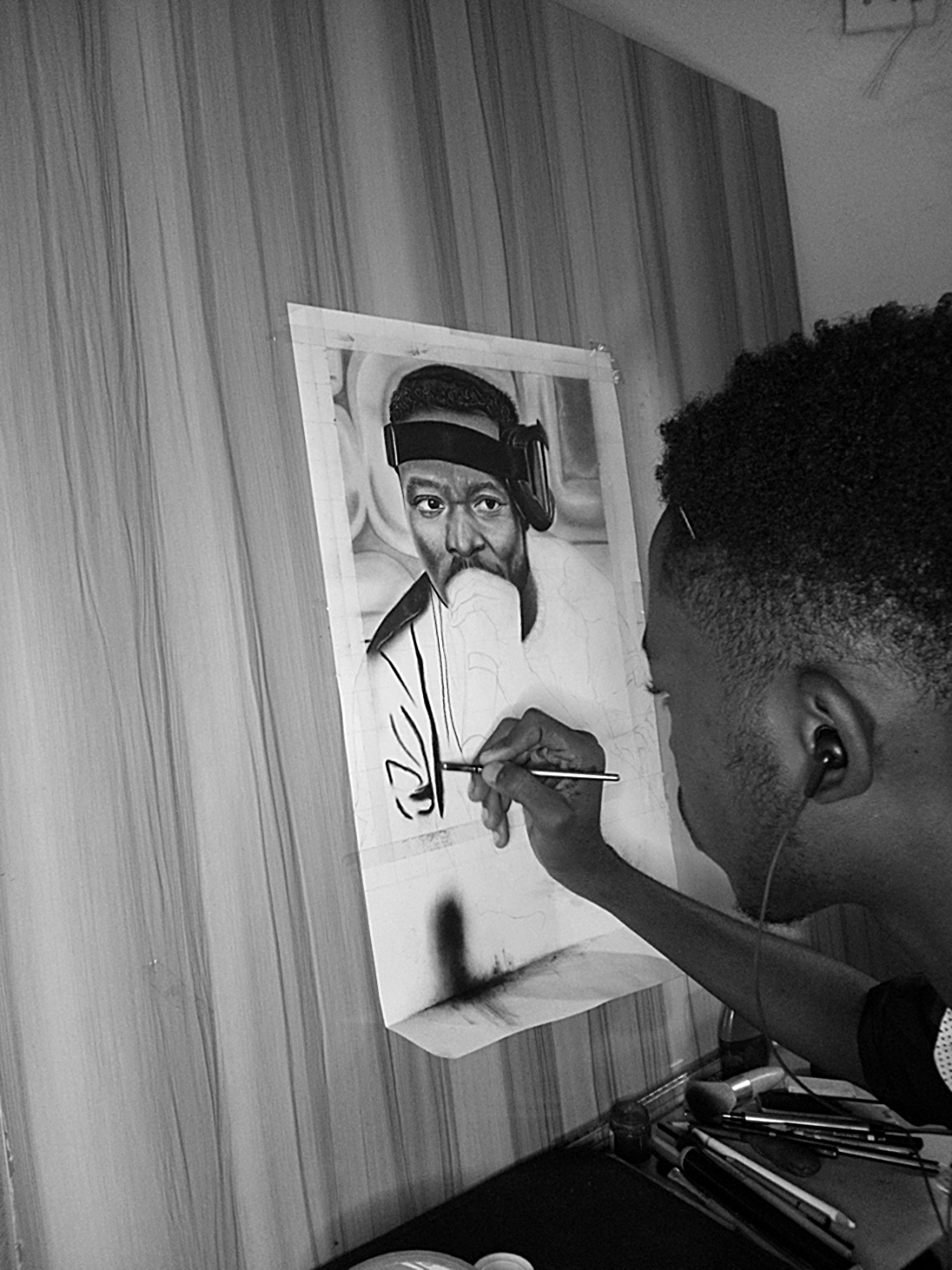 Young man painting a portrait on a canvas, wearing headphones, with a curtain background.
