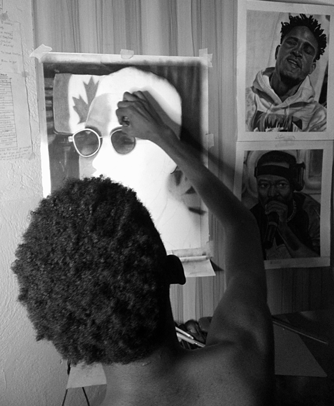Person with curly hair adjusting sunglasses on a portrait of a face with a maple leaf, surrounded by posters on the wall.