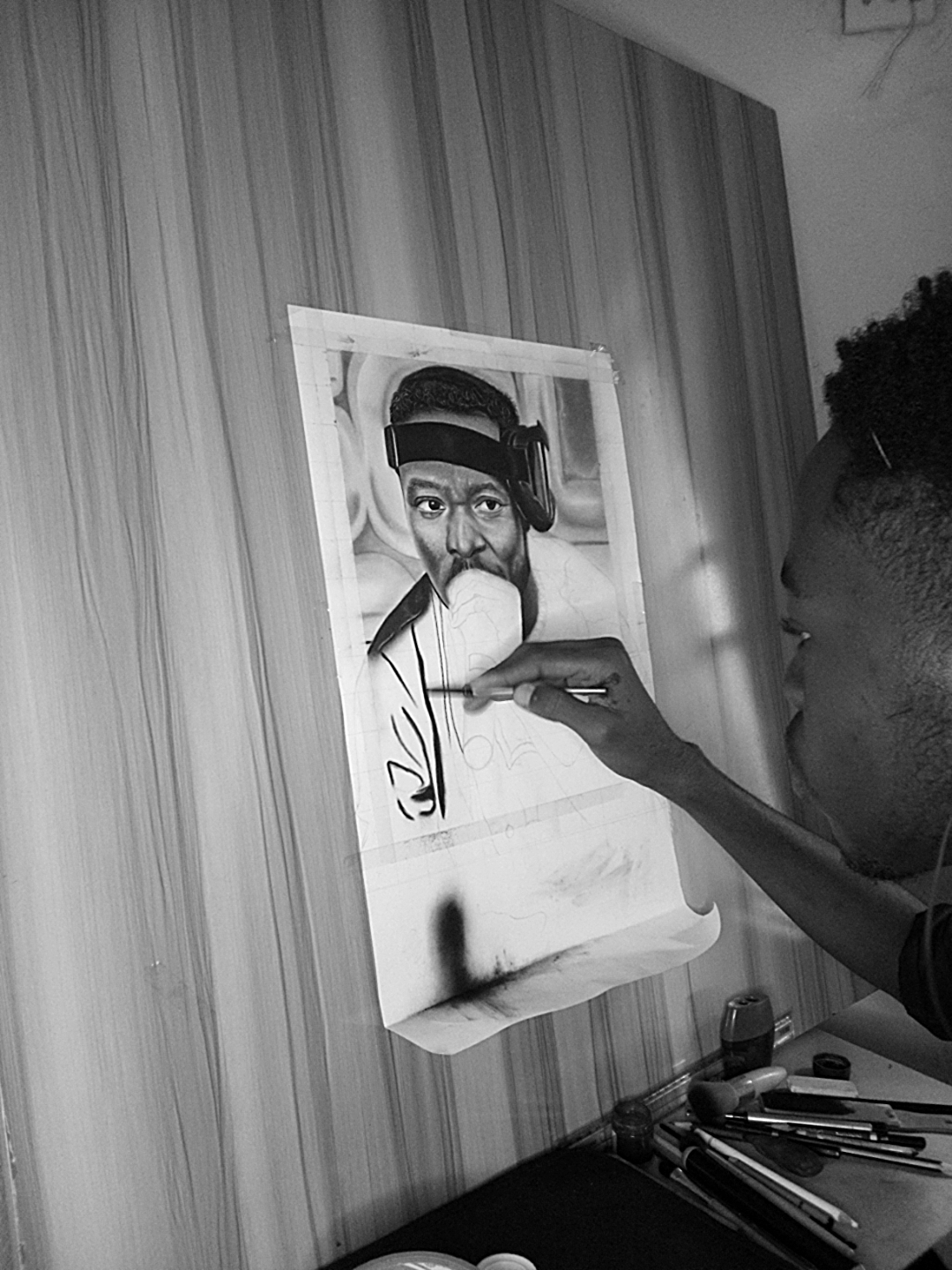 Person painting a portrait of a woman with glasses and a headscarf on a canvas, with art supplies nearby.