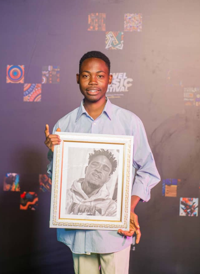 Young person holding a framed portrait drawing, standing in front of a dark background with colorful abstract designs.