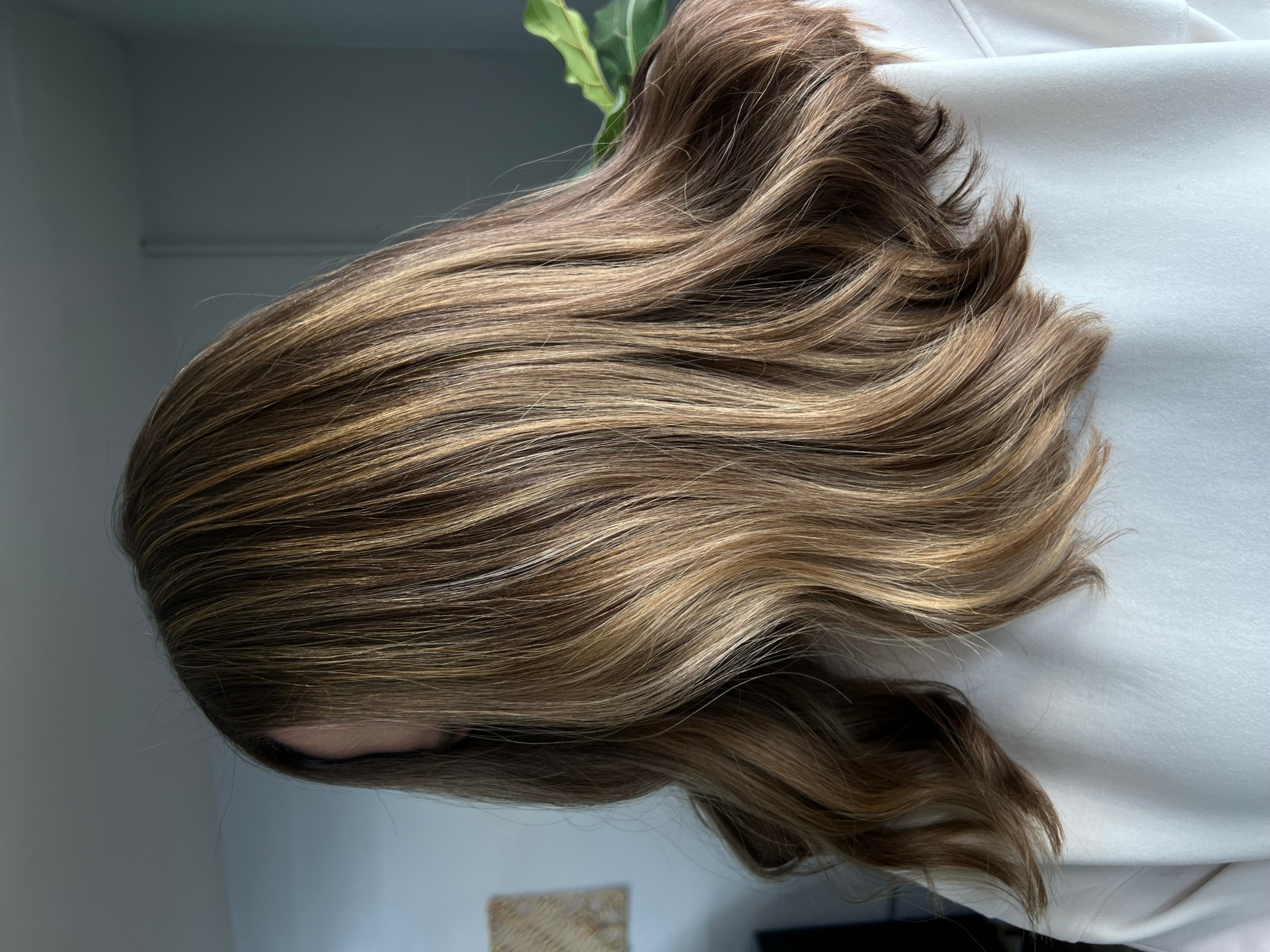 Side view of wavy, light brown hair with blonde highlights, resting on a white surface.