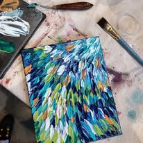 Paintbrush and a colorful abstract painting on a messy art table.