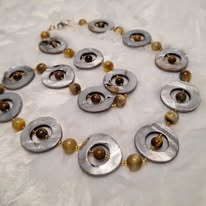 Necklace with circular silver and gold beads, featuring eye-shaped pendants, arranged on a light surface.