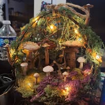 Decorative mushroom arrangement with lights, moss, and branches in a basket, illuminated softly in a cozy setting.