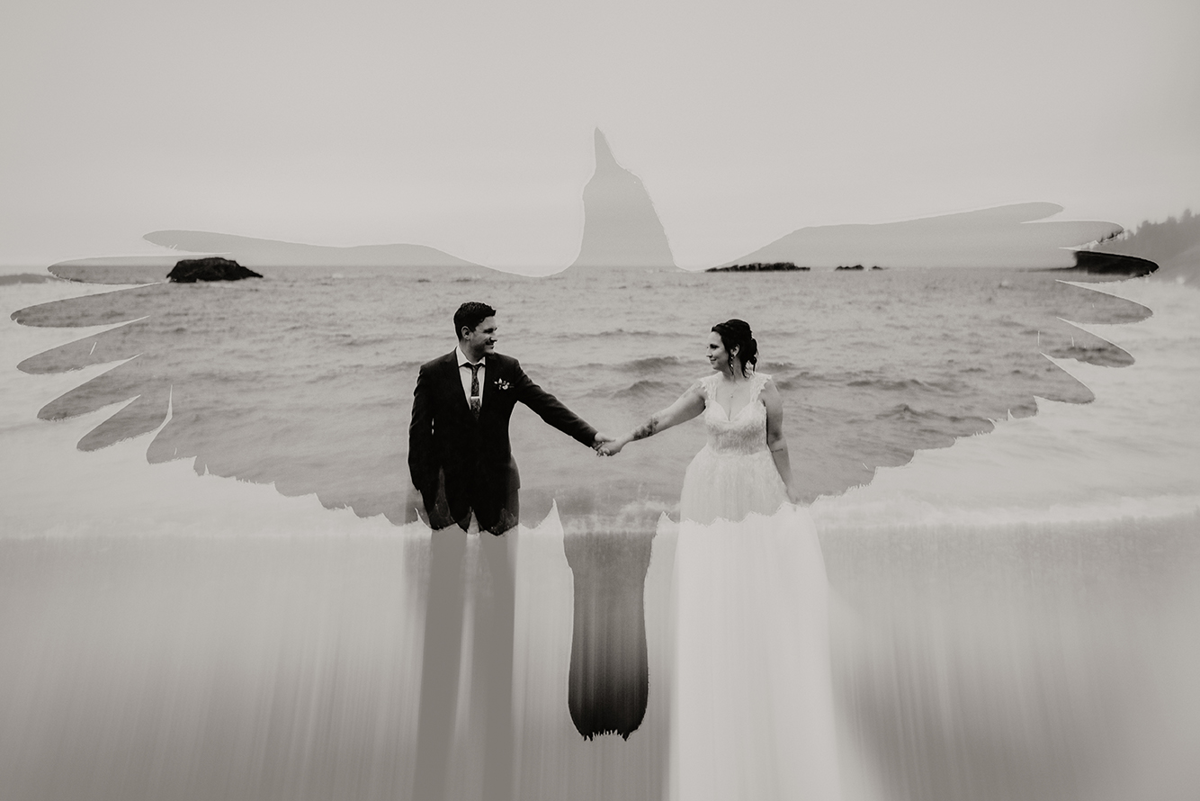 A couple in wedding attire holding hands in water with a distant mountain in the background, mirrored reflection below, black and white.
