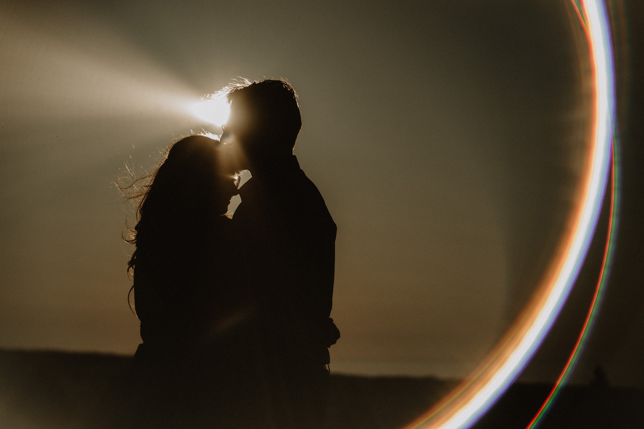 Silhouette of a couple kissing against a sunset, with a bright light behind them and a circular light pattern on the right.