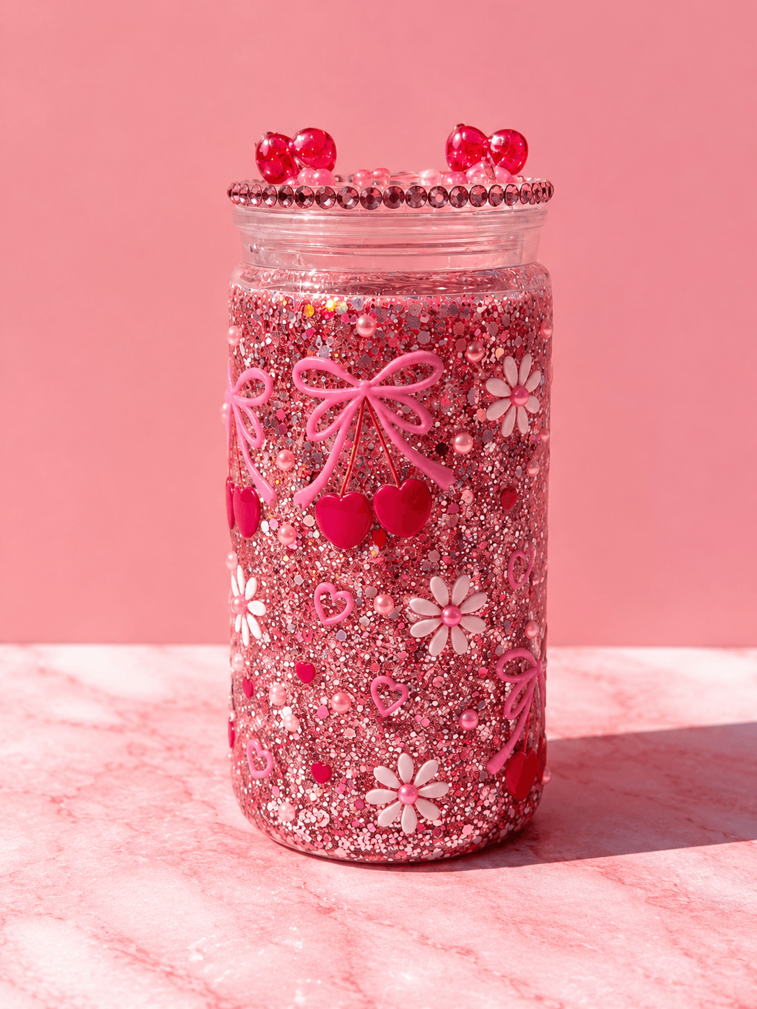 Decorated jar with pink glitter, cherries, and floral patterns on a pink background.