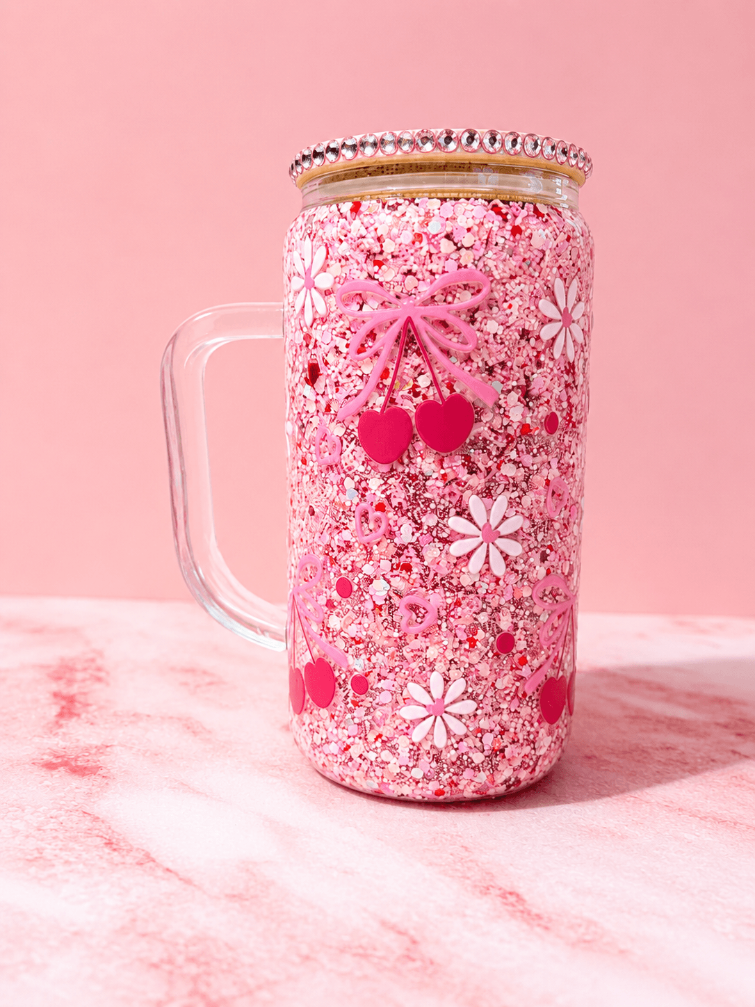 A jar decorated with pink and white floral patterns, cherries, and a beaded lid, on a pink background.