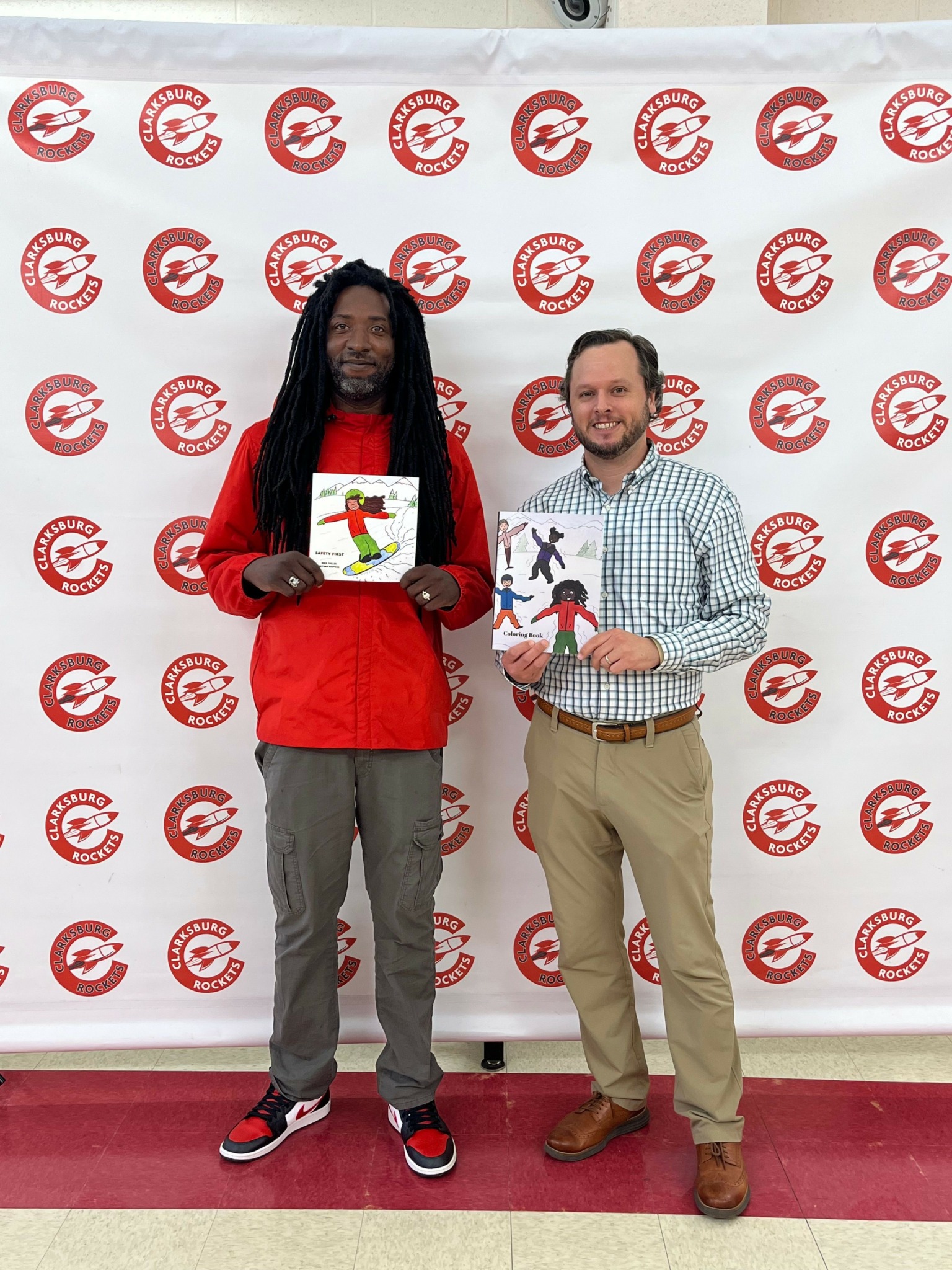 Two people standing in front of a backdrop with red and white logos, holding a certificate and a trophy.