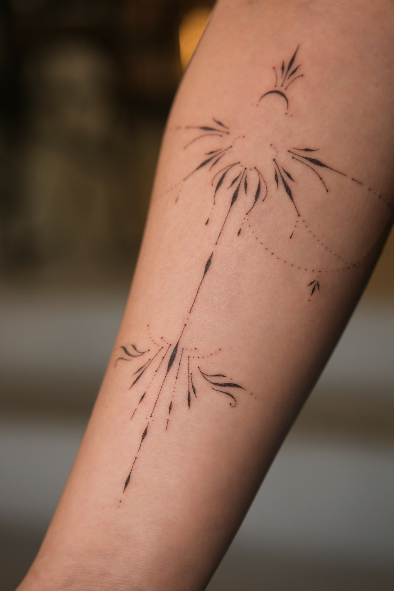 A minimalist black ink tattoo of a firework explosion on a person's forearm, with lines and dots radiating outward.