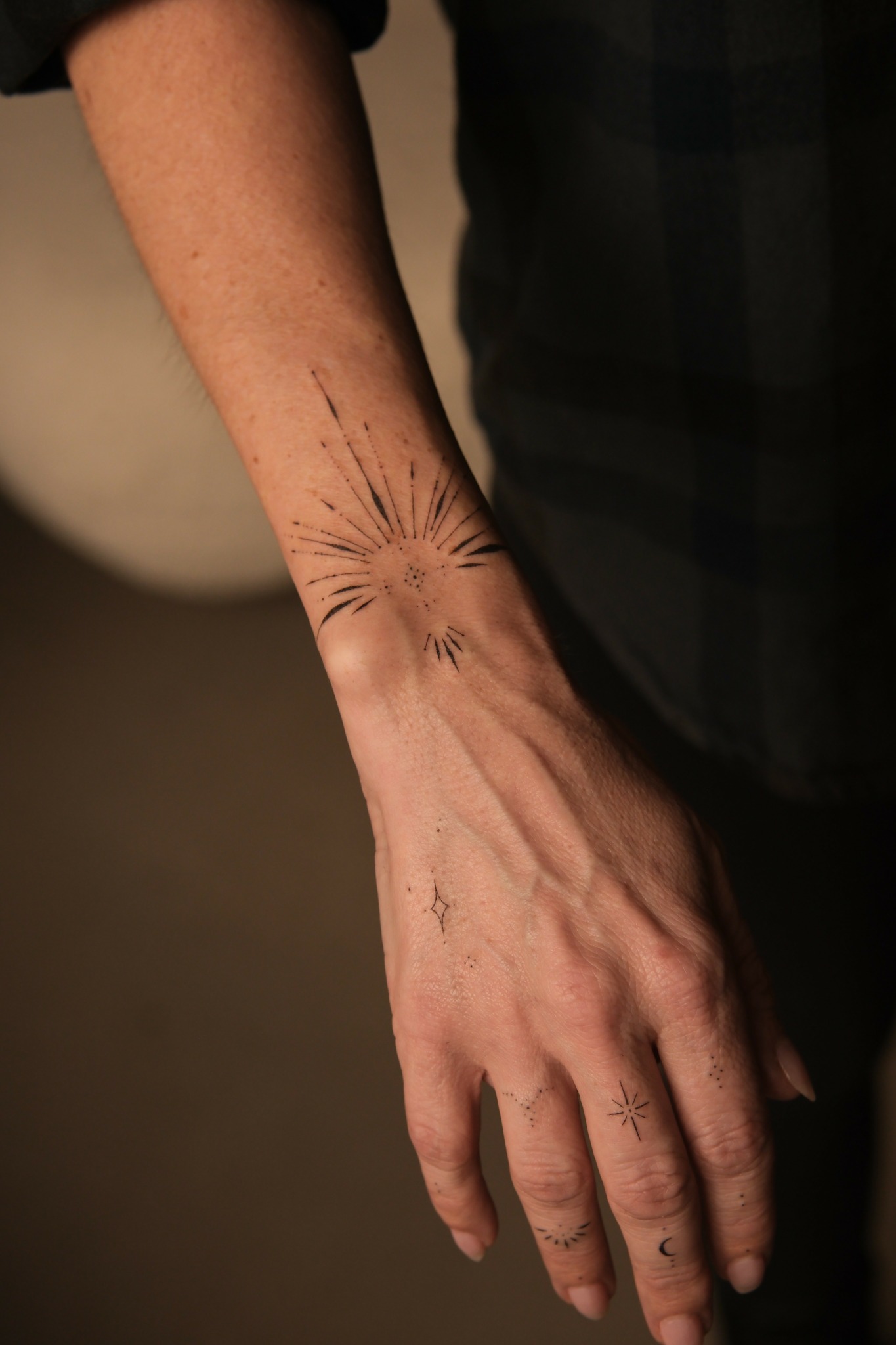Person's arm with a tattoo of a sunburst design on the wrist, hand relaxed, background blurred