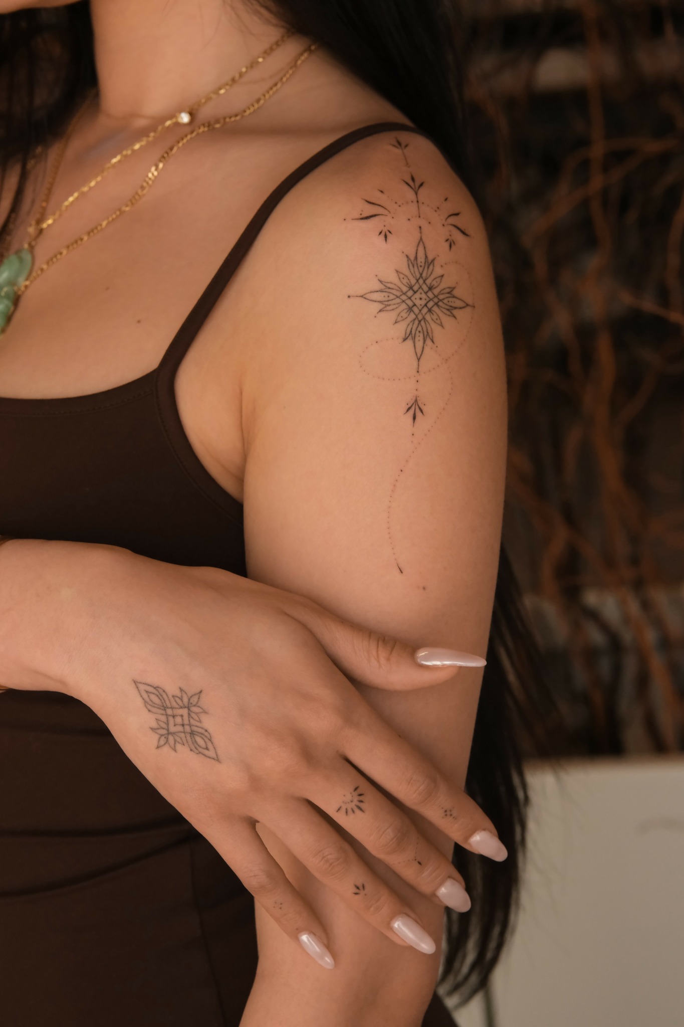Person with a starburst tattoo on shoulder and a smaller tattoo on hand, wearing a black top, in a dimly lit setting.