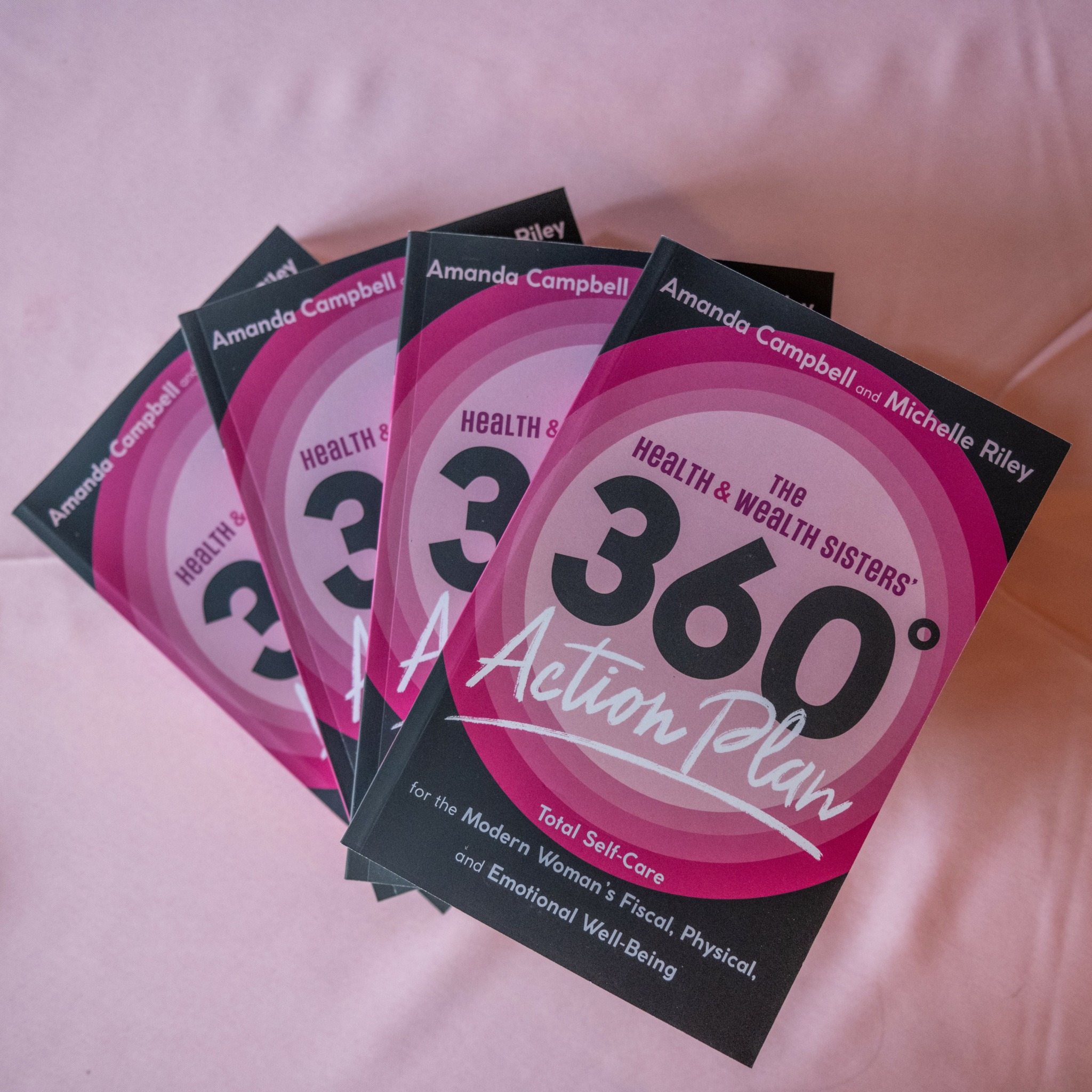 Four copies of a book titled 'The 360° Action Plan' are fanned out on a pink surface.