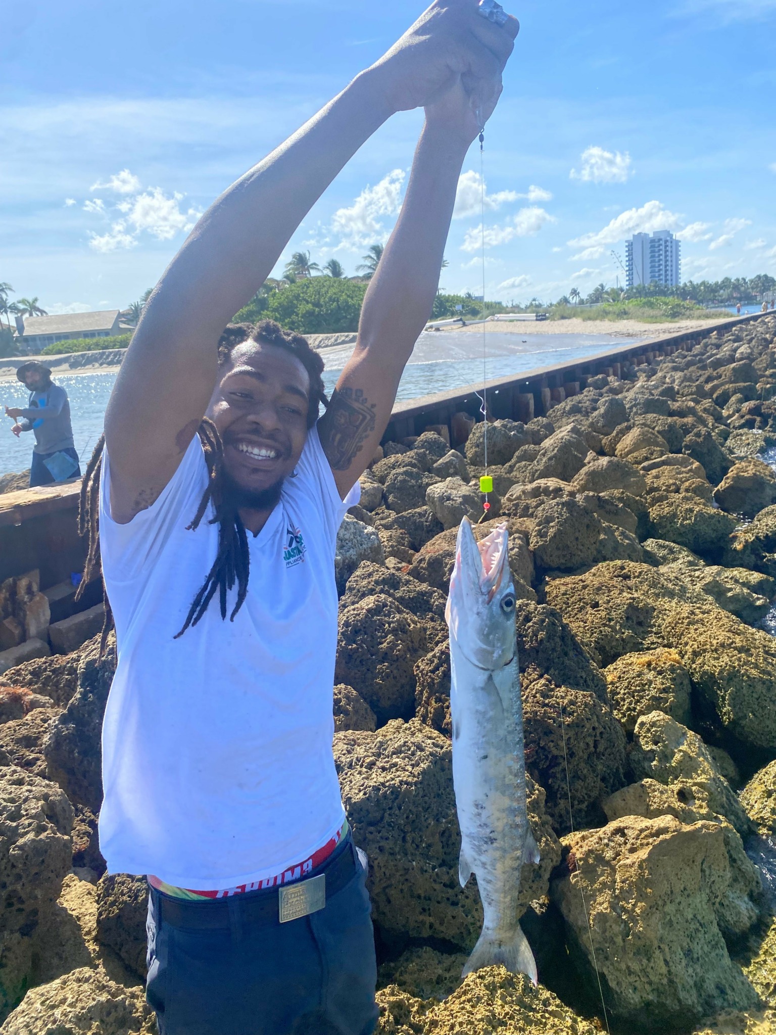 Person holding a fish on rocks near water, with a bridge and city skyline in background.