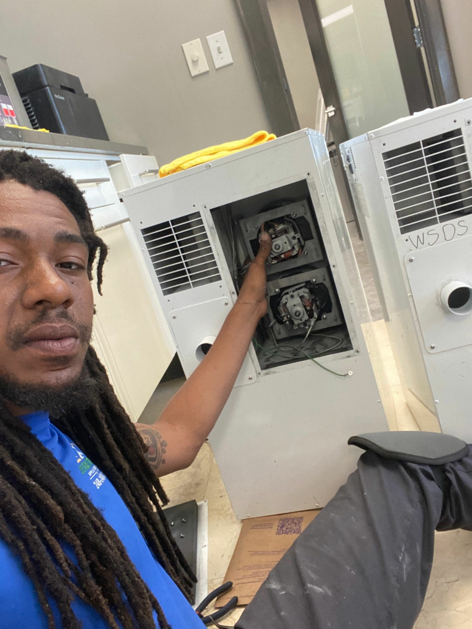 Person with long dreadlocks working on electrical panel, with tools and equipment nearby.