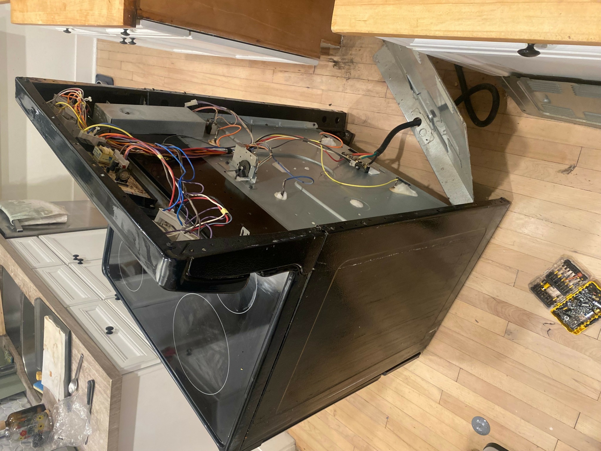 Open dishwasher with visible internal components and wiring, placed on a wooden floor in a kitchen.