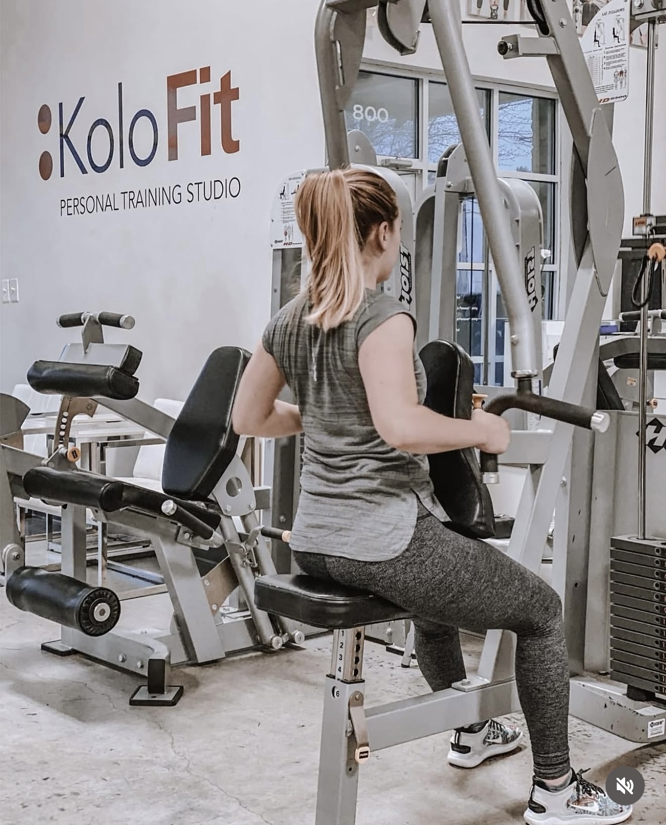 Woman sitting on a gym machine at KoloFit personal training studio, with exercise equipment around her.