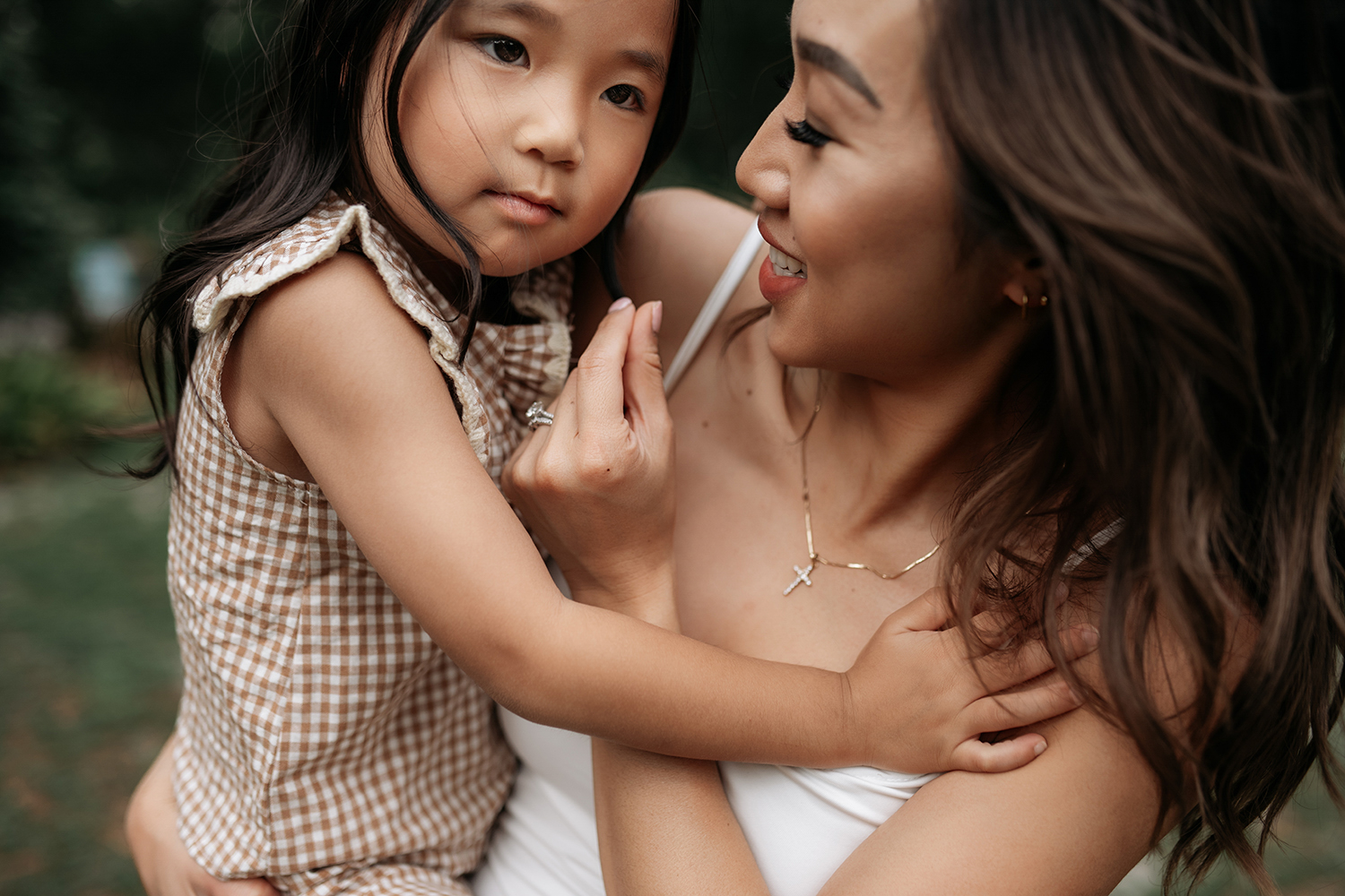 Woman and young girl outdoors, close-up, woman smiling, girl looking at her, woman holding girl, natural setting