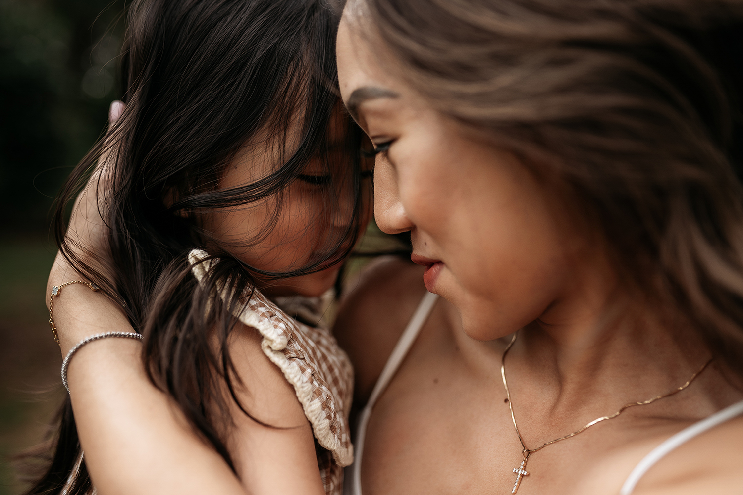 Two women face each other closely, with their foreheads touching and eyes closed, showing an intimate moment.