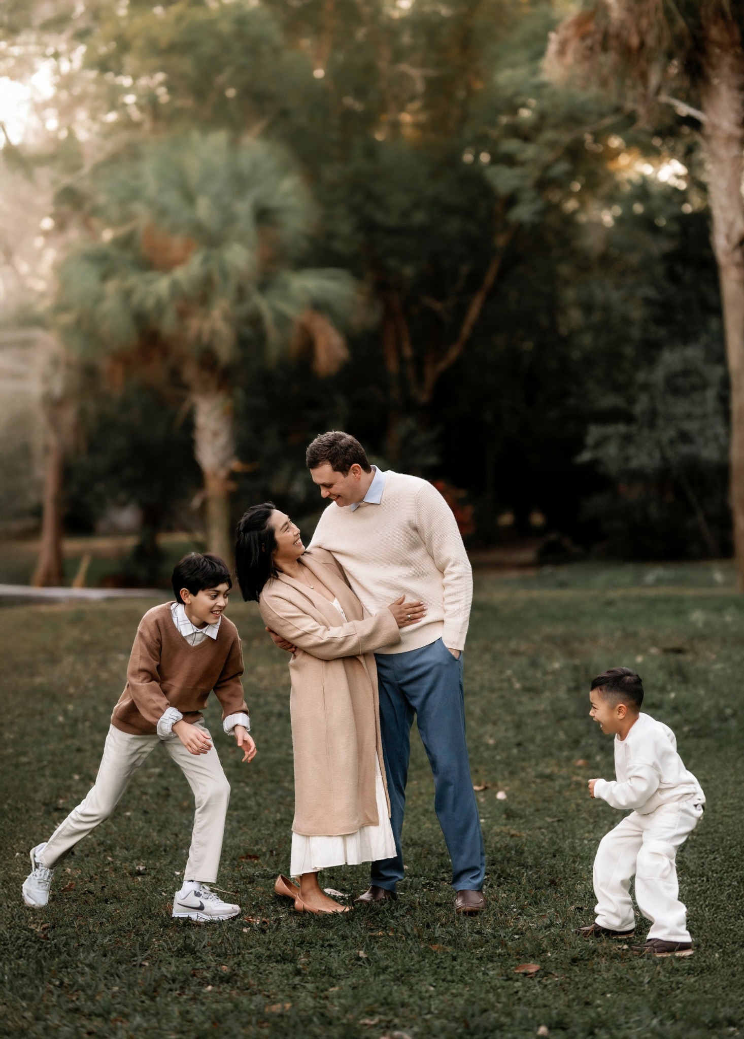 Family of four standing and playing on grass in park with trees in background.