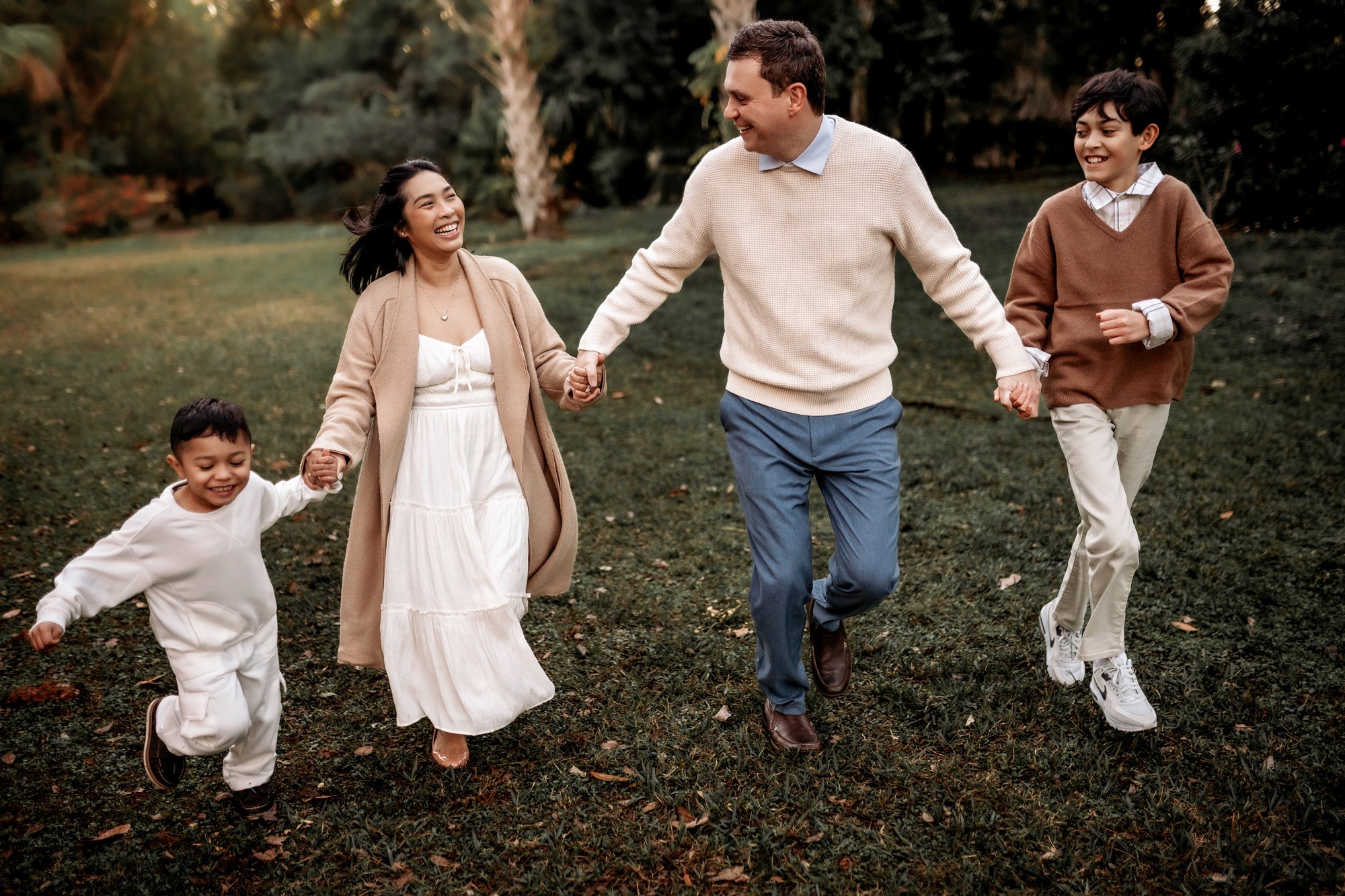 Family of four holding hands and walking outdoors in a park, smiling and enjoying the day.