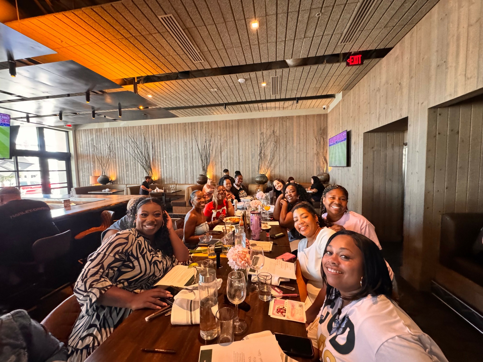 Group of people sitting at a long table in a restaurant, smiling and enjoying a meal.