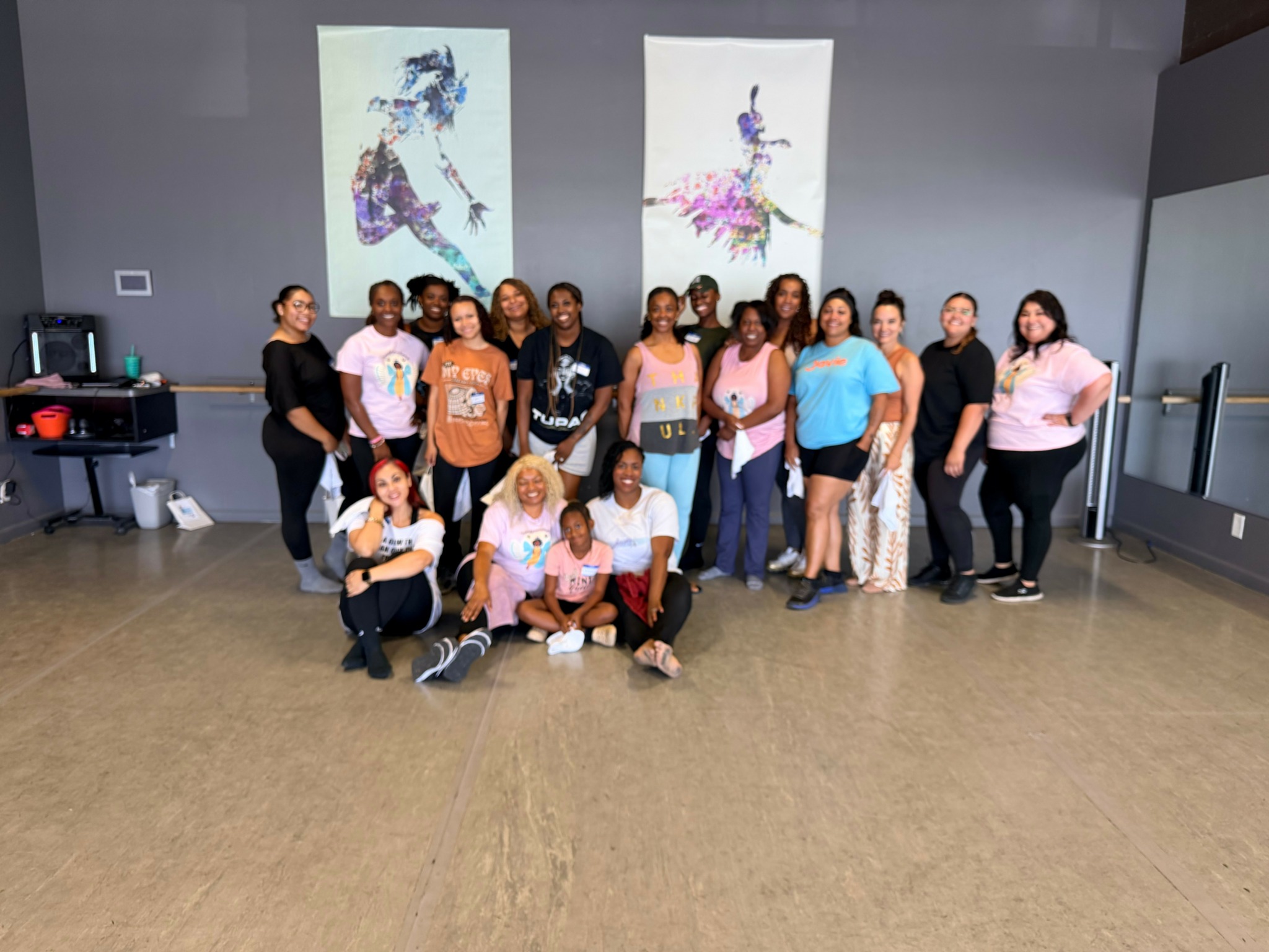 Group of 15 people standing and sitting in a room with two large colorful abstract art pieces on the wall behind them.