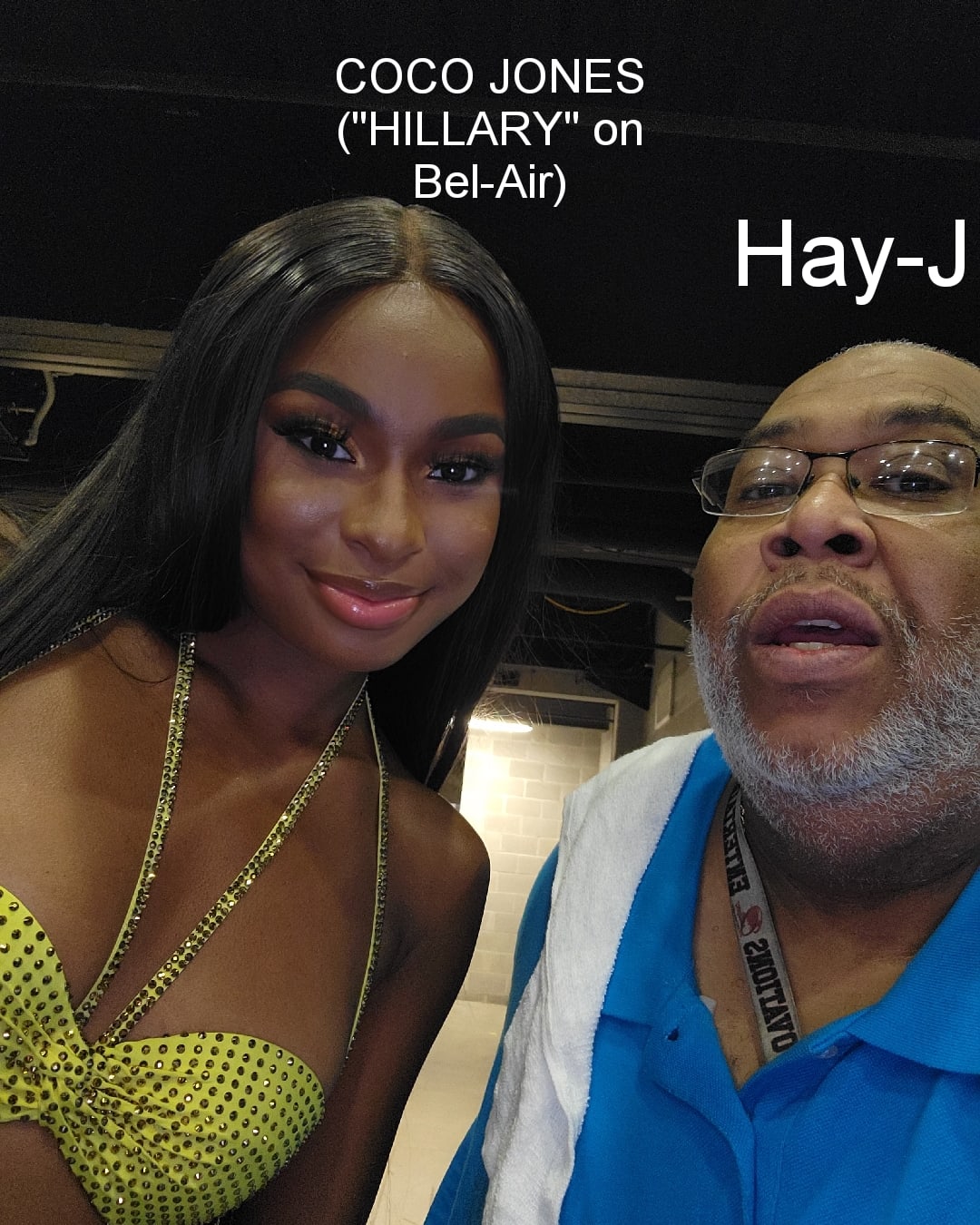 Coco Jones and a man pose for a photo, Coco wears a yellow dress with a necklace, man wears glasses and a blue shirt.