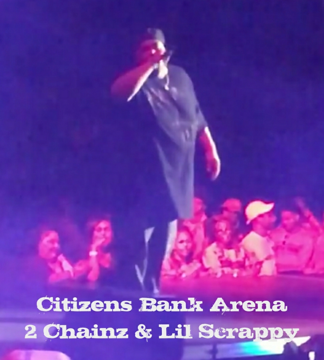 Person standing on stage with microphone, audience in background, at Citizens Bank Arena, 2 Chainz and Lil Scrappy perform.