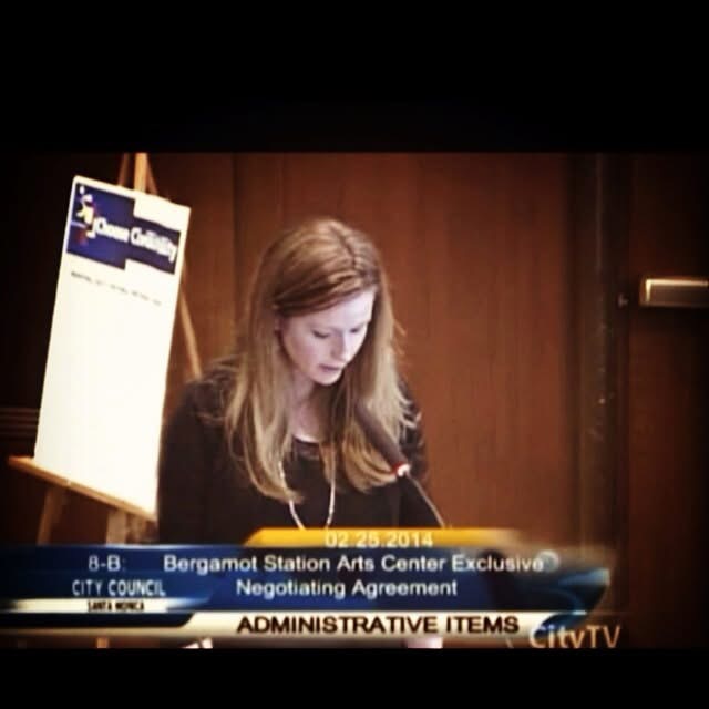 Woman with long hair looking down at a document in a wood-paneled room, with a sign and a news ticker at the bottom.