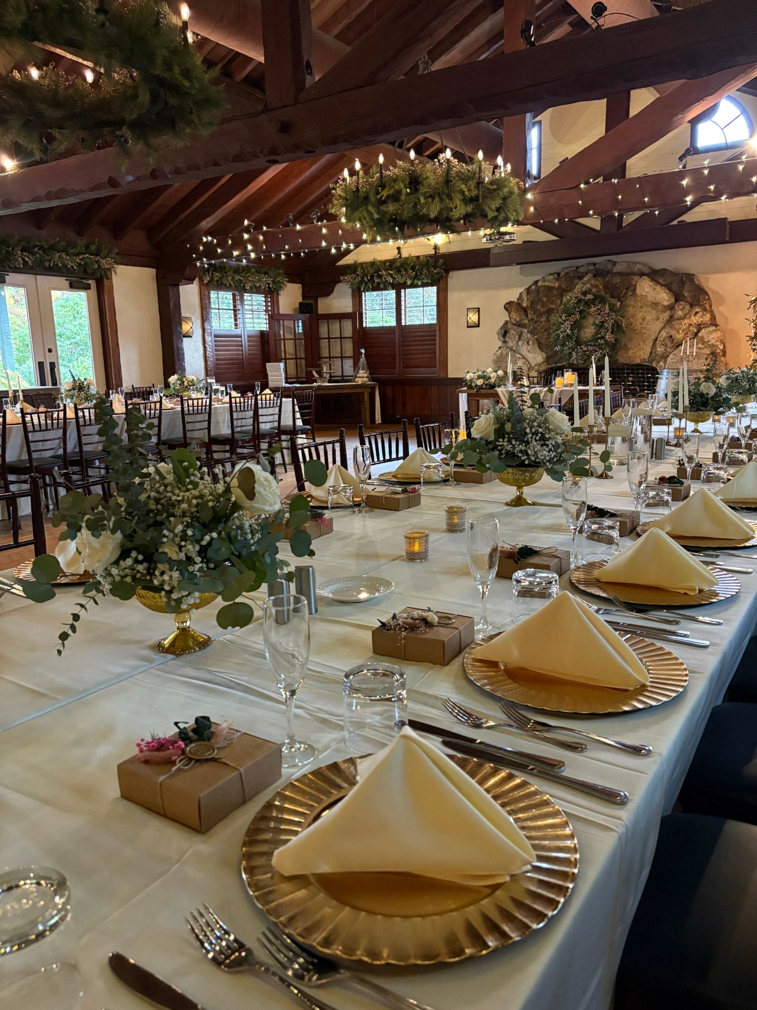 Elegant banquet table set with yellow napkins, floral centerpieces, and gold-rimmed plates in a decorated venue.