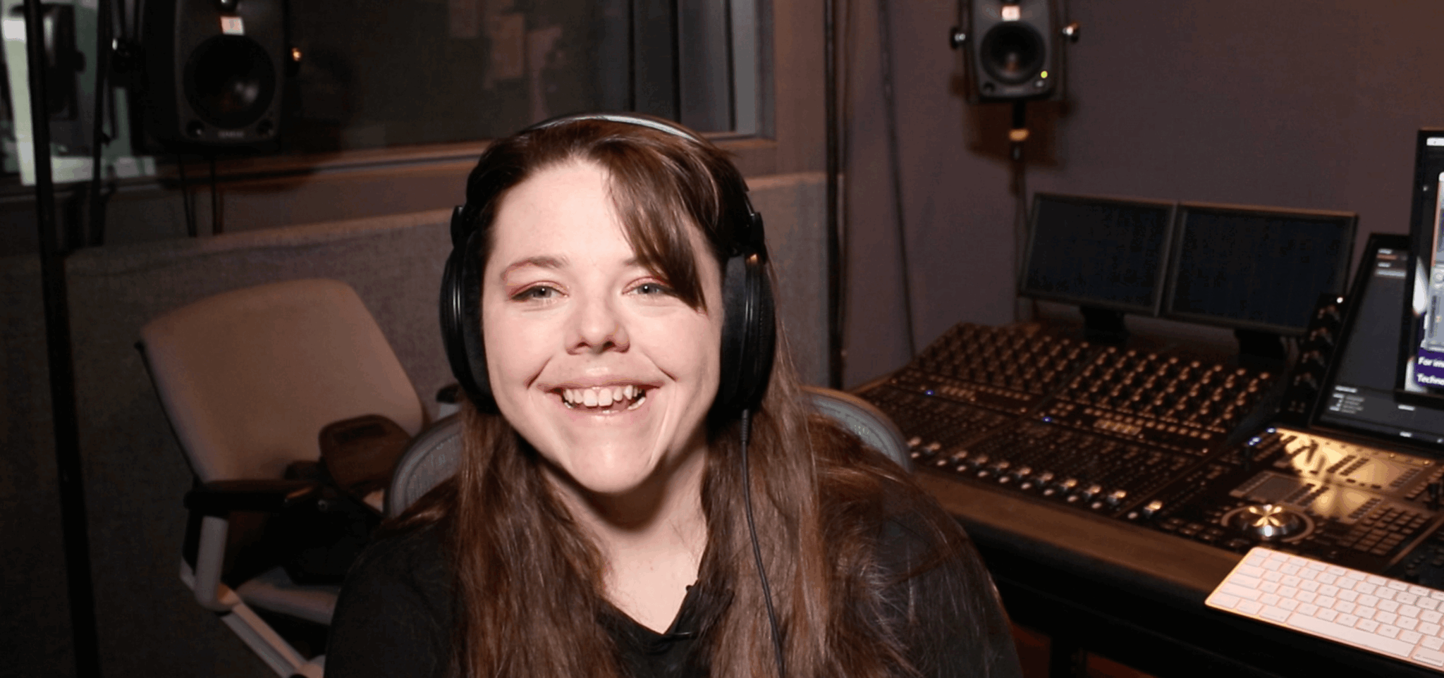 Young woman with long hair wearing headphones smiling in a recording studio.