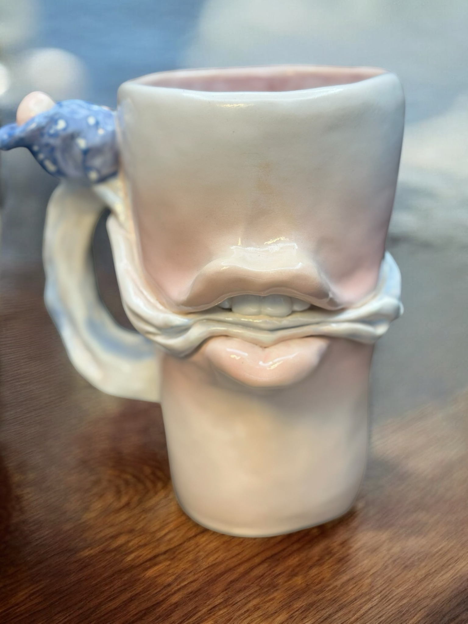 Ceramic mug with a face design, featuring a handle on the left, placed on a wooden surface.