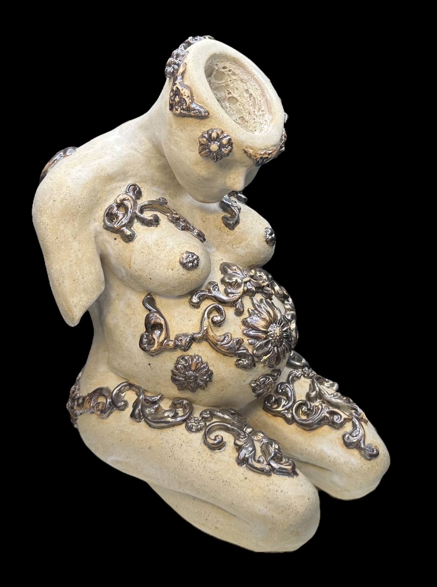 Sculpture of a seated female figure with decorative metal embellishments, missing head, against a black background.