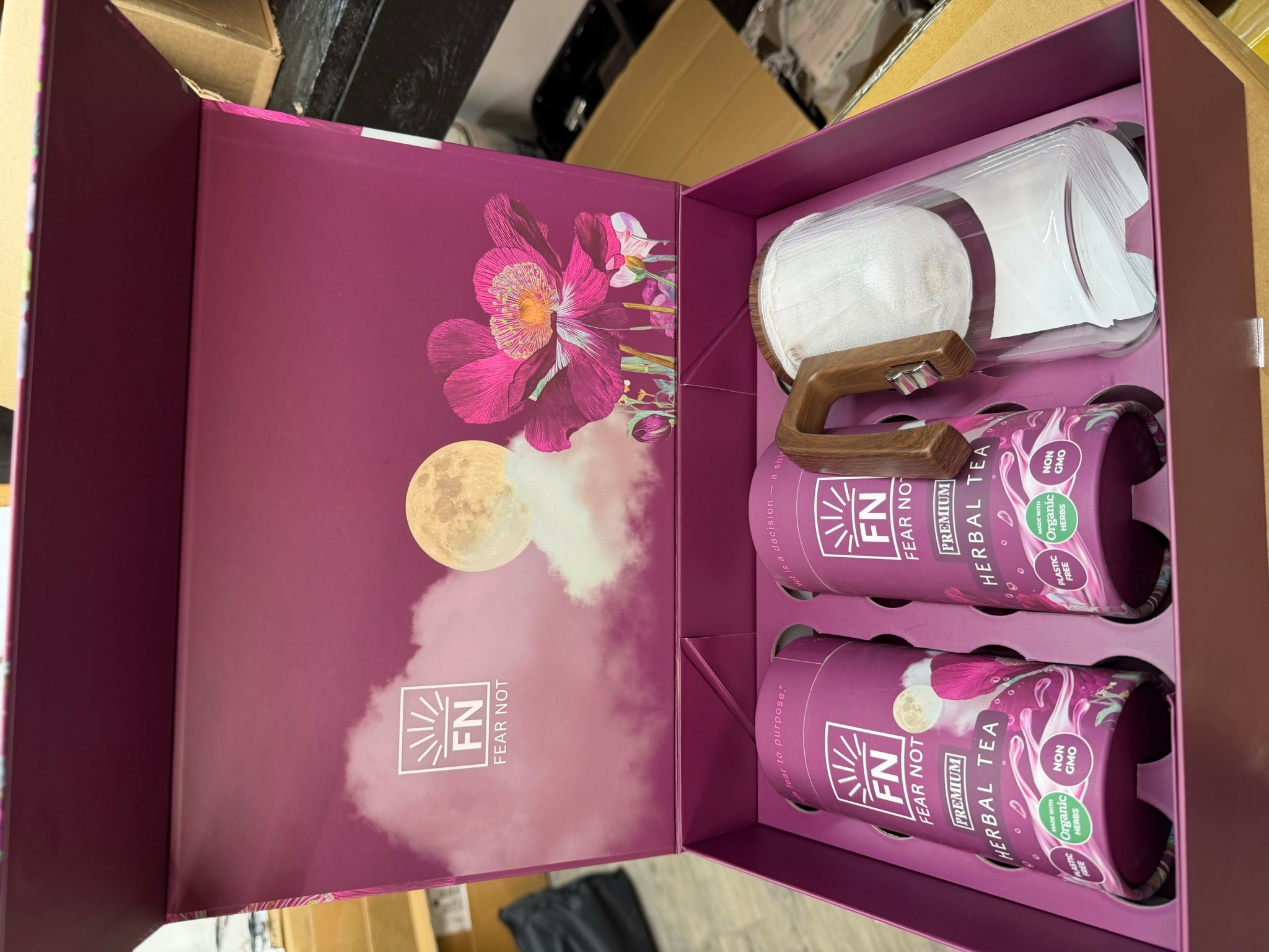 Open pink box with floral design, containing white rolled towels and pink bottles of personal care products.