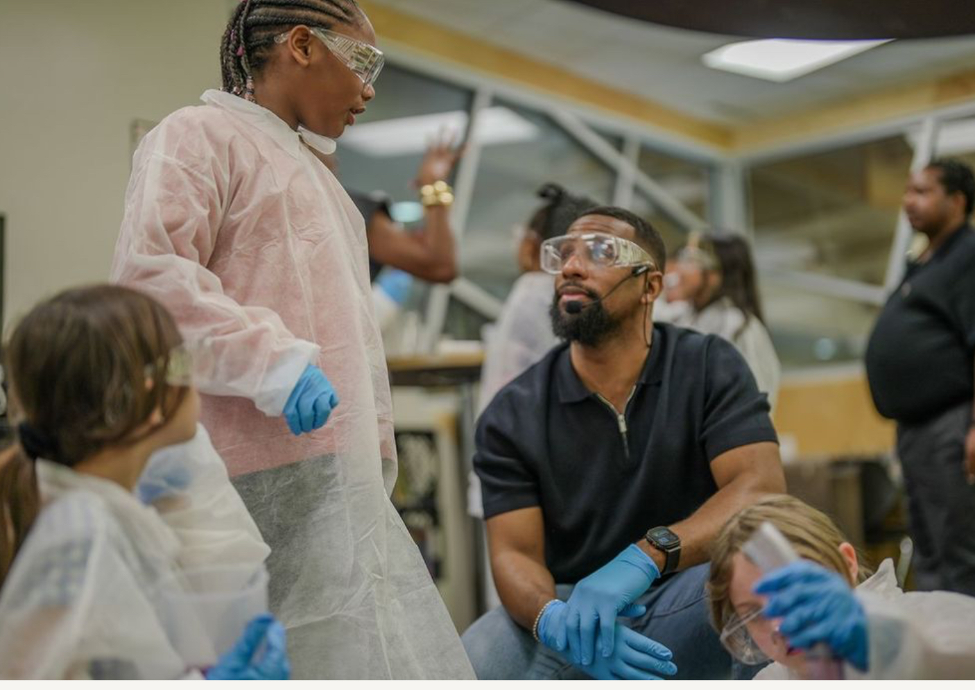 Medical professionals and a man wearing protective gear and gloves in a clinical setting, engaging in a discussion.