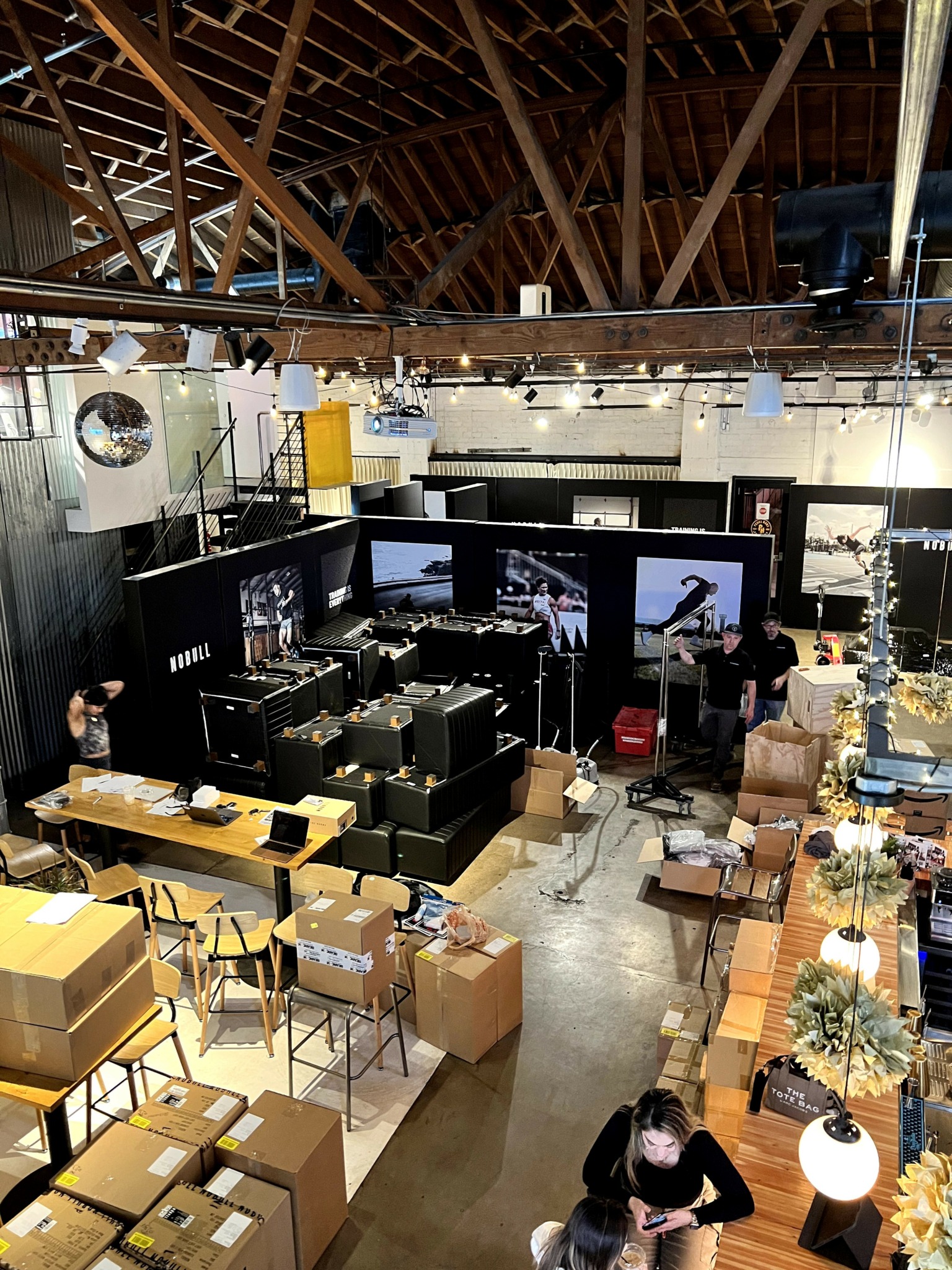 Indoor space with stage, seating, and boxes, possibly a warehouse or event venue, with a person sitting on the floor.
