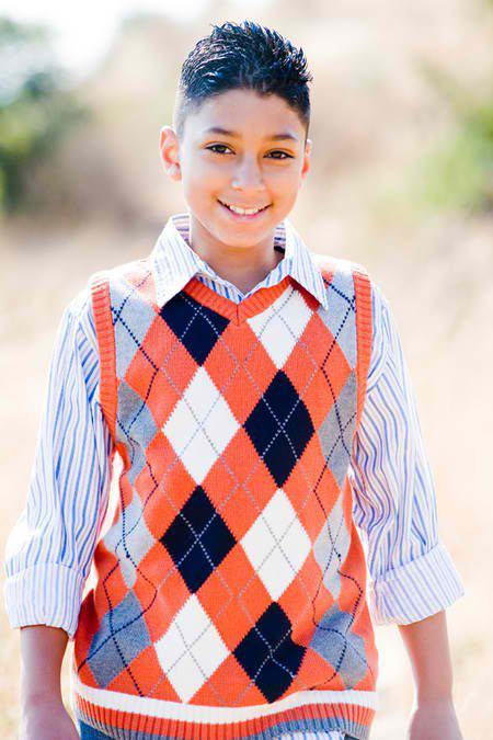 Smiling boy in striped shirt and argyle sweater vest outdoors, blurred background