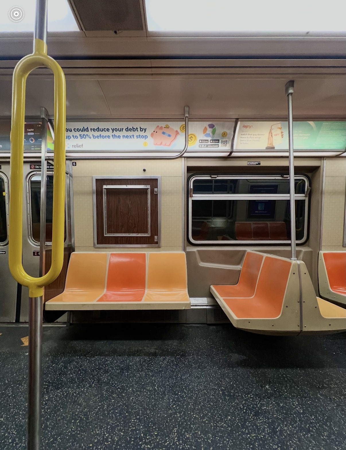 Empty subway train interior with orange seats, window, and advertisement above seats.