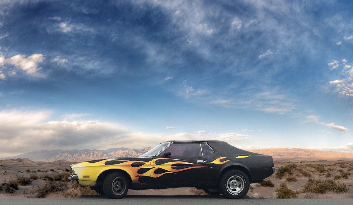 Black car with yellow flame decals parked in a desert landscape under a partly cloudy sky.
