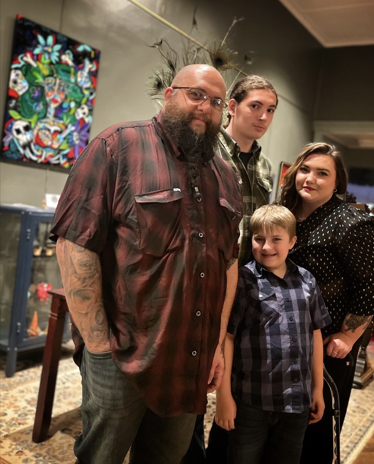 Four people standing indoors, with a colorful artwork on the wall behind them.