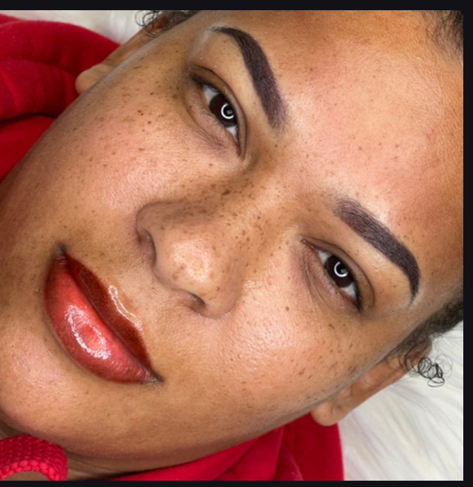 Close-up of a woman's face with makeup, freckles, and dark eyebrows, lying down with a red garment visible.