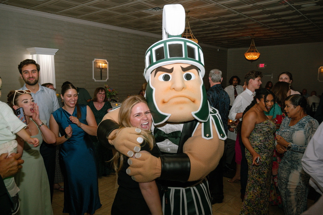 Person hugging a large mascot costume of a Roman soldier at a party with people in the background.