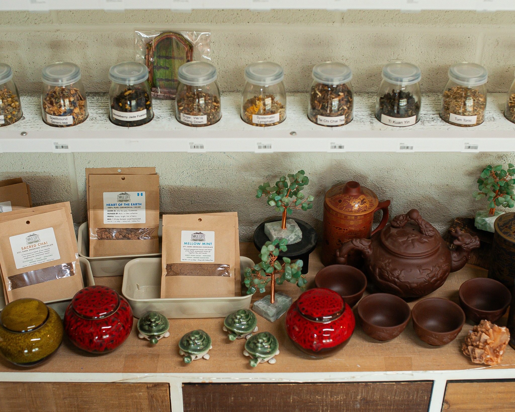 Display of jars, bags, and teapots on shelves and table, with plants and decorative items, in a shop setting.