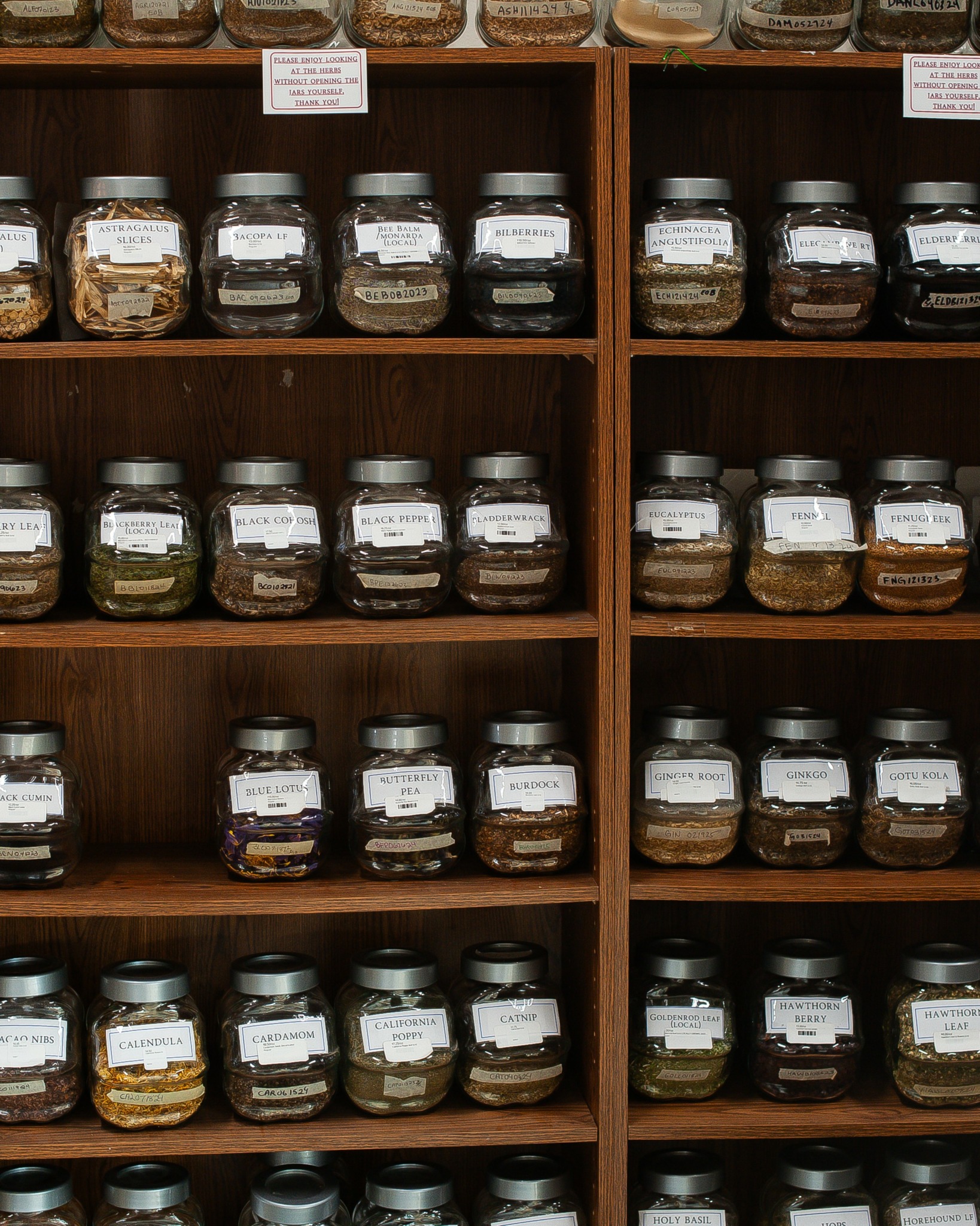 Wooden shelves filled with glass jars containing various spices or herbs, labeled and organized neatly.