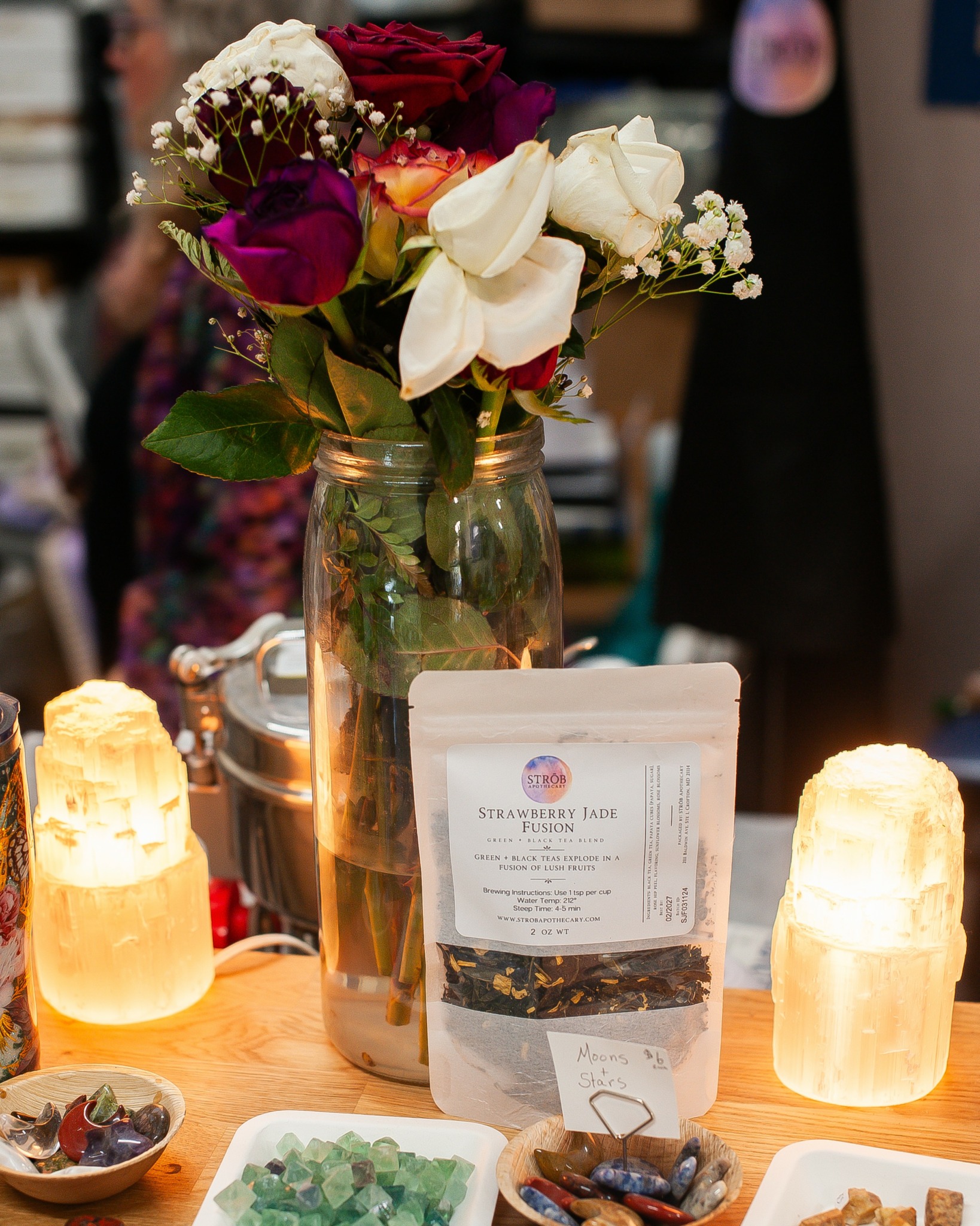 Flower bouquet in a jar, illuminated candles, and a menu on a wooden table at an indoor event.