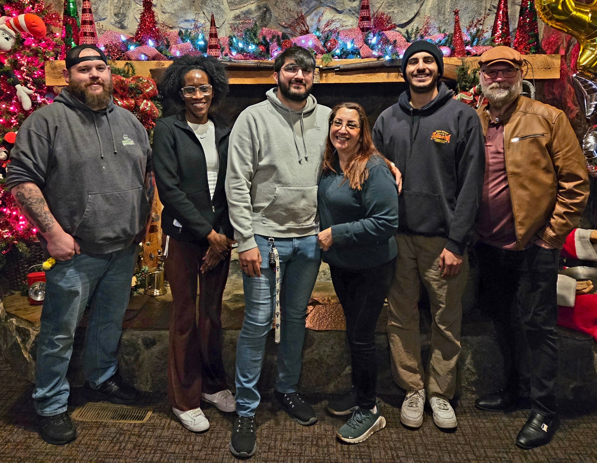 Group of six people standing in front of a decorated Christmas display, smiling, indoors.